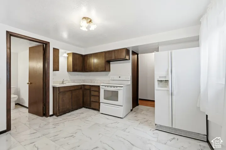 Kitchen featuring dark-finish wood cabinetry, stone-patterned tile flooring, white appliances, and semi-flush mount ceiling lighting