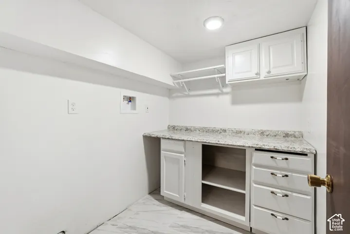 Utility room featuring white cabinetry, stone-finish countertops, built-in open shelving, tiered drawers, and wall-mounted storage rack