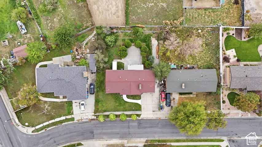 Aerial perspective of the property featuring a paved driveway, concrete rear patio, and established landscaping