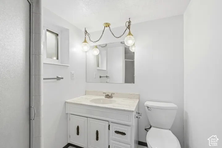Bathroom featuring a vanity with stone-finish countertop, integrated basin, decorative hanging light fixture, and large wall mirror