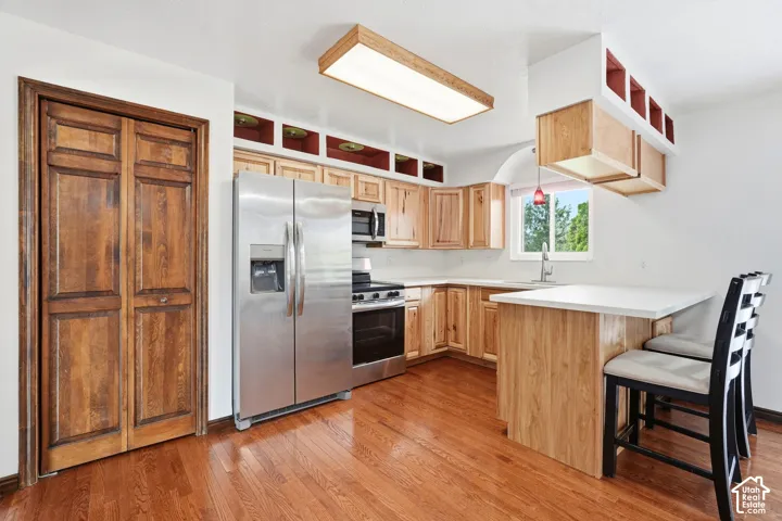 Kitchen featuring wood-finish cabinetry, stainless steel appliances, a peninsula with an attached counter, wood-finish flooring, and a double-door closet with wood paneling