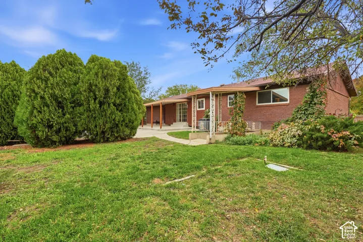 Single-story brick exterior featuring a covered patio, concrete walkway, and expansive lawn with mature landscaping