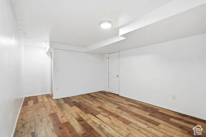 Interior room featuring neutral white walls, wood-finish flooring, and a flush-mount overhead light fixture