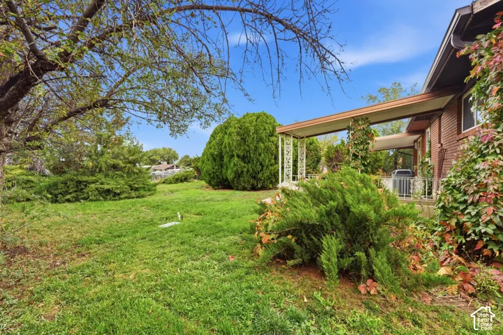 Brick exterior featuring a covered patio, decorative metal support columns, mature trees, and landscaped shrubbery