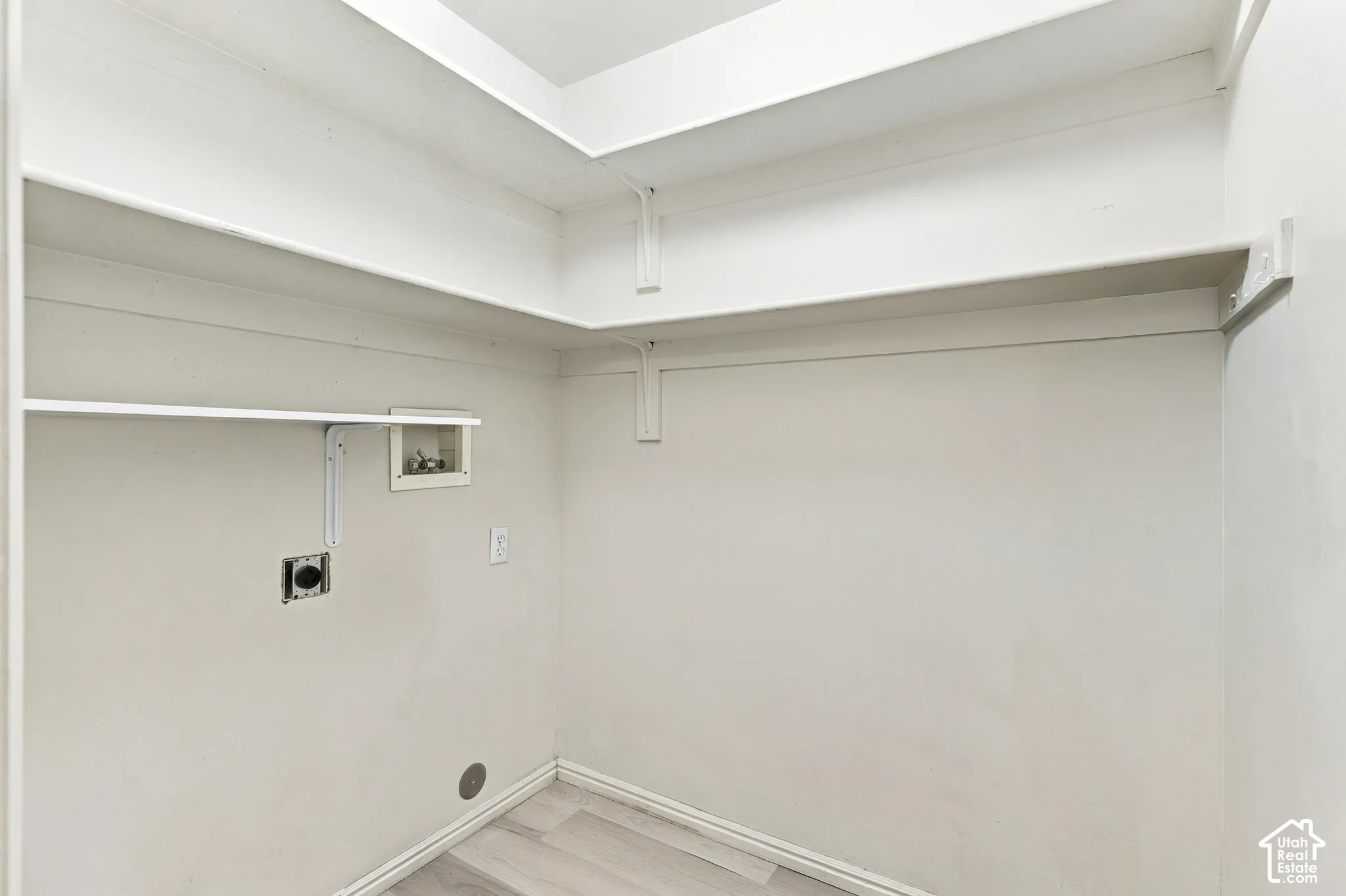 Utility closet with integrated shelving, appliance hookups, and wood-finish flooring