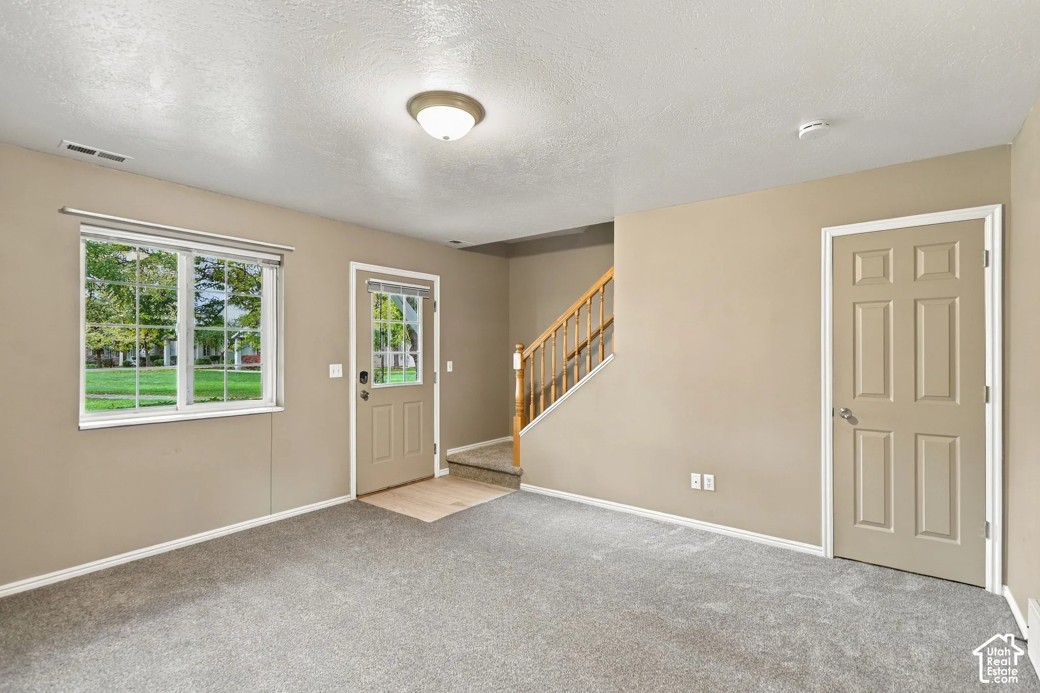 Bright, open great room with neutral carpeting and soft-toned walls, accented by large multi-pane windows flooding the space with natural light