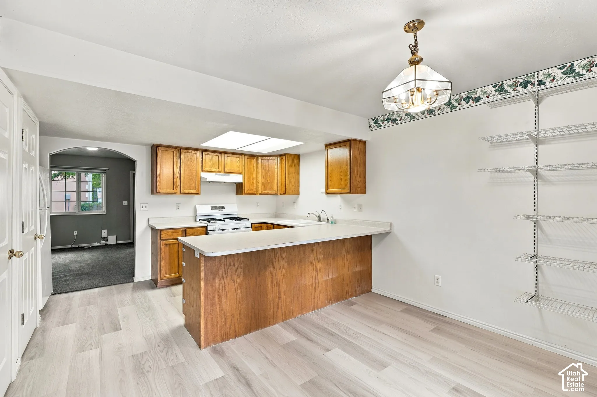Spacious kitchen featuring wood-finish cabinetry, a large center island with white countertop, stainless steel appliances, pendant lighting, and light wood-finish flooring throughout