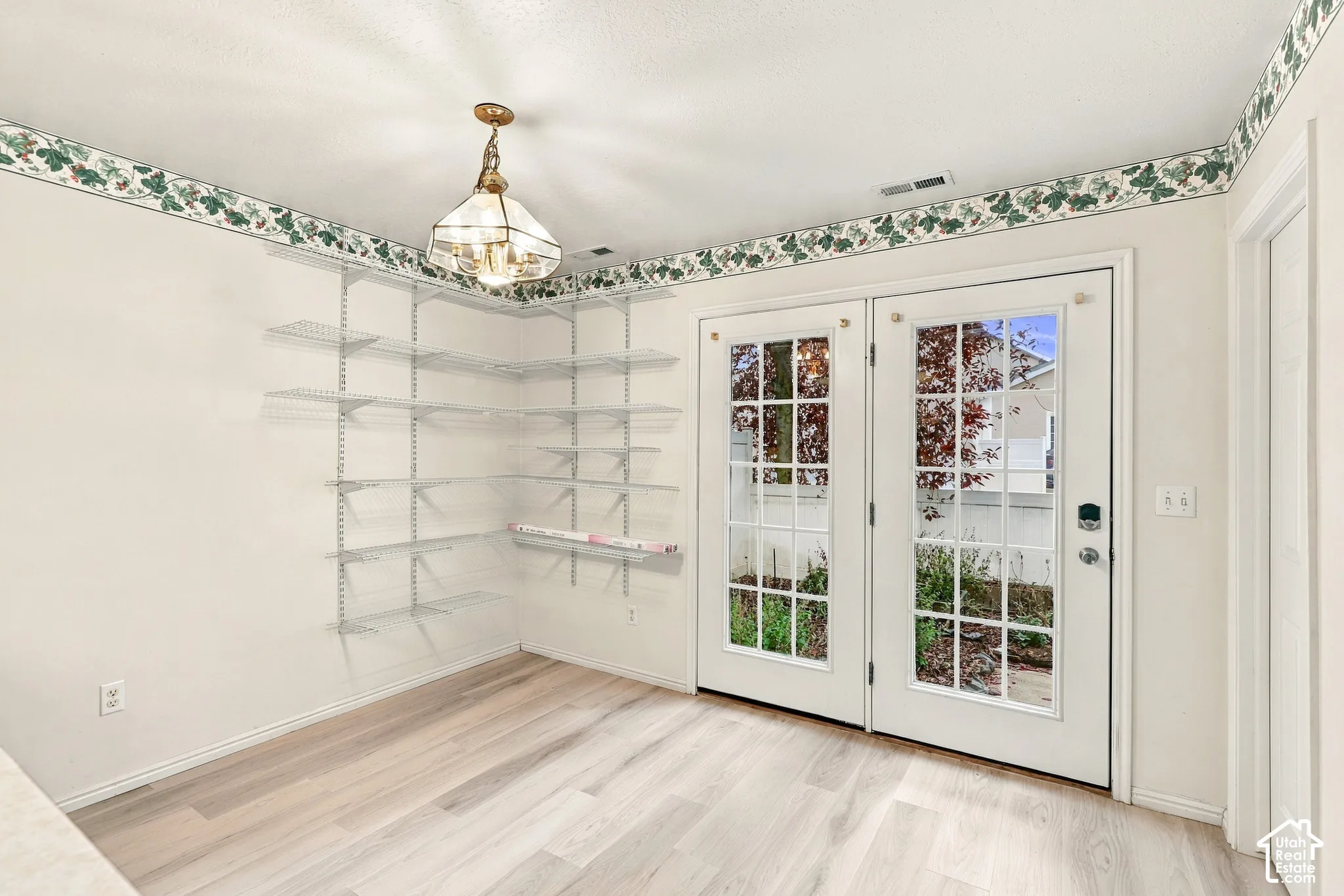 Double French doors with divided lites, corner wire shelving, wood-finish flooring, and a decorative ceiling light fixture