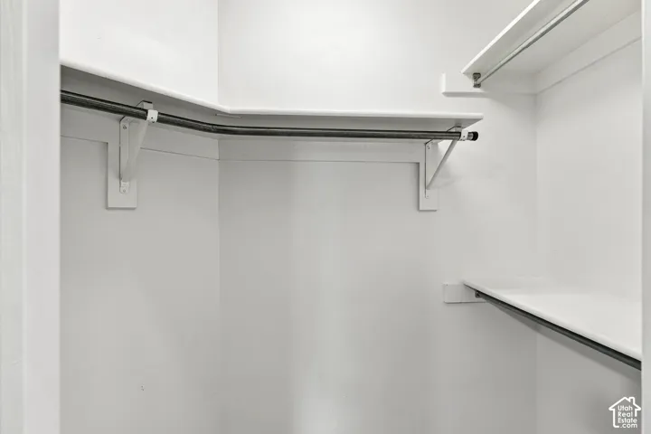 Spacious walk-in closet featuring dual hanging rods with adjustable brackets, shelving system, and white painted walls for maximum storage and organization