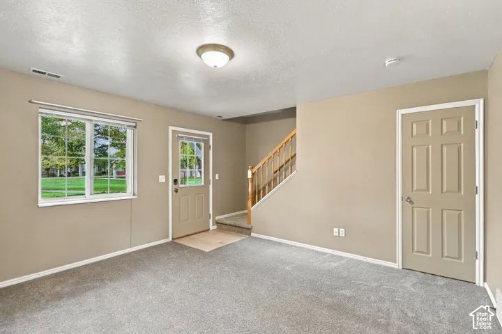 Bright, open great room with neutral carpeting and soft-toned walls, accented by large multi-pane windows flooding the space with natural light