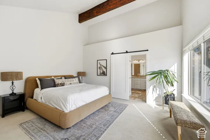 Vaulted ceiling with exposed wood beam, large windows, white walls, and a barn door entry to the bathroom