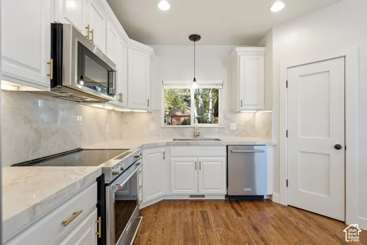 White cabinetry with gold-finish hardware, stainless steel appliances, light-toned countertop and backsplash, wood-finish flooring, and recessed lighting