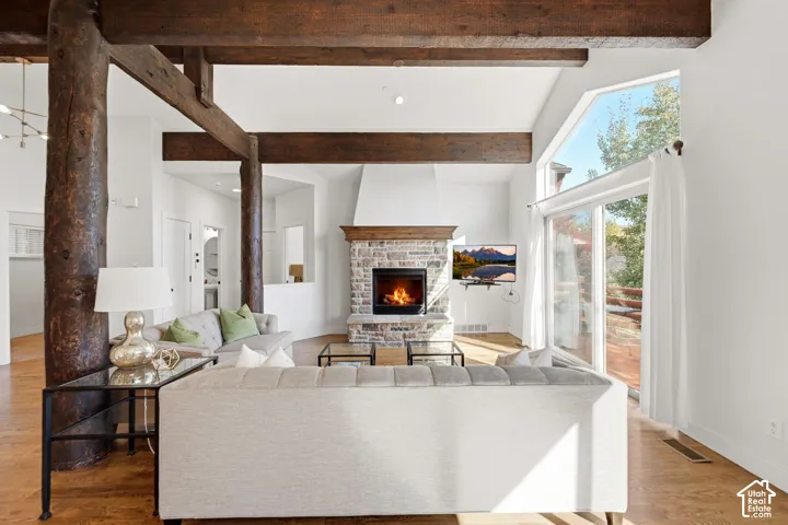 Vaulted ceilings with exposed wood beams, stone-clad fireplace, and wood-finish flooring