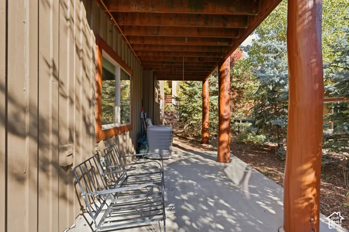 Covered outdoor area featuring concrete flooring, exposed wood beam ceiling, natural wood support pillars, and board-and-batten siding