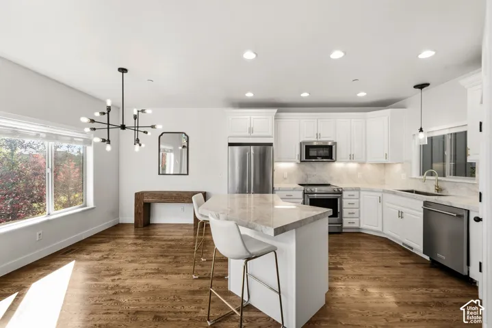 Open-concept kitchen and dining area featuring wood-finish flooring, white cabinetry, integrated stainless steel appliances, and a central island with countertop seating