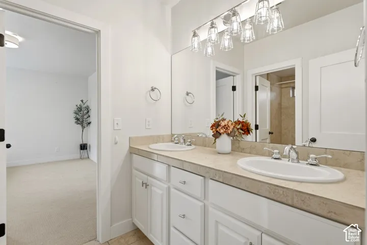 Dual sink vanity with white cabinetry, polished chrome fixtures, and overhead multi-bulb lighting