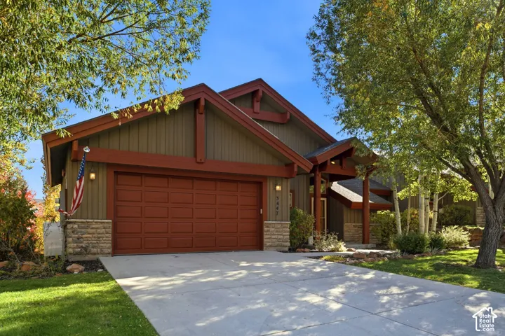 Craftsman-style exterior with stone veneer accents, an attached garage, covered entry, and mature landscaping