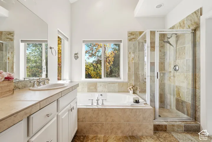 Dual-sink vanity with light-toned countertop, soaking tub with tile surround, walk-in shower with glass enclosure, and tiled flooring