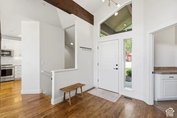 Hardwood flooring in entryway, vaulted ceiling with exposed beam, white paneled entry door with sidelight, large transom window, and adjacent built-in cabinetry with countertop