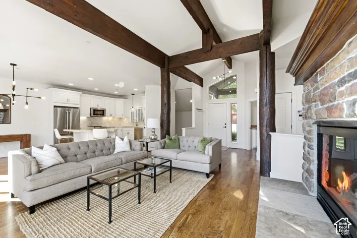 Exposed wood beam ceilings, stone fireplace, hardwood flooring, white kitchen cabinetry, and stainless steel appliances