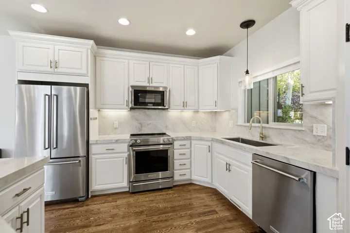 White cabinetry, stainless steel appliances, marble-patterned countertops and backsplash, wood-finish flooring, and recessed lighting