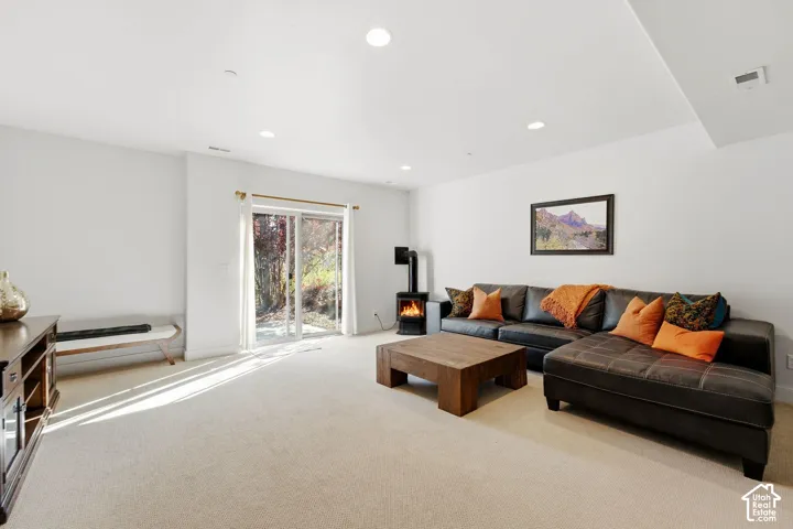 Recessed lighting illuminates a spacious room featuring a floor-to-ceiling sliding glass door, plush carpet flooring, and a modern freestanding fireplace