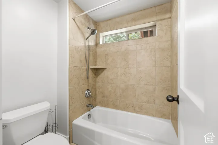 Tub and shower combination with tan tile surround, built-in shelf, and small transom window