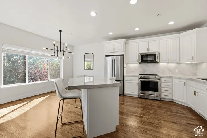 Open-concept kitchen with white cabinetry, stainless steel appliances, and wood-finish flooring
