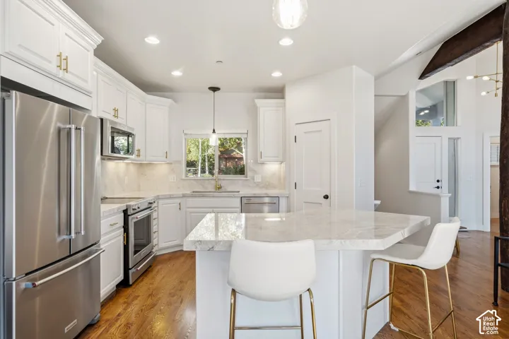 White cabinetry with gold-finish hardware, stainless steel appliances, and wood-finish flooring