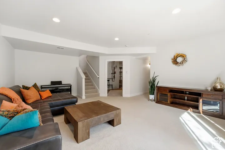 Recessed ceiling lighting, carpeted flooring, staircase with white railing, built-in media console, and a separate doorway