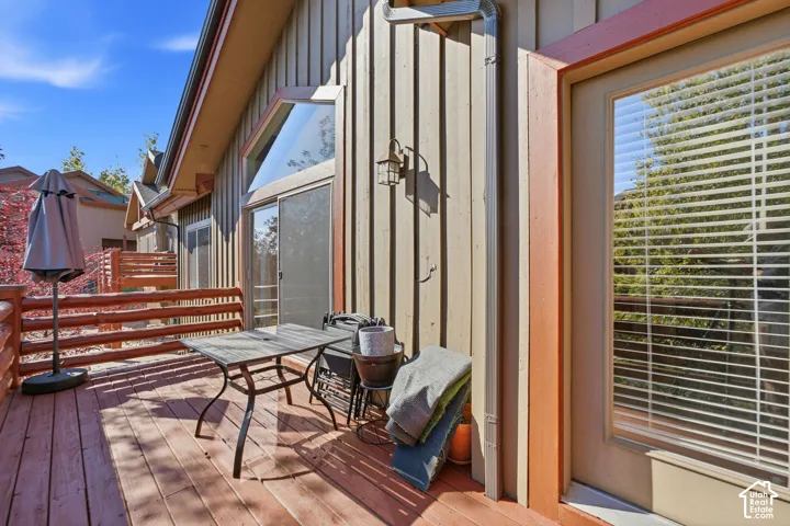 Wood-plank deck with log railing, board and batten siding, exterior wall sconce, and sliding glass door with transom window