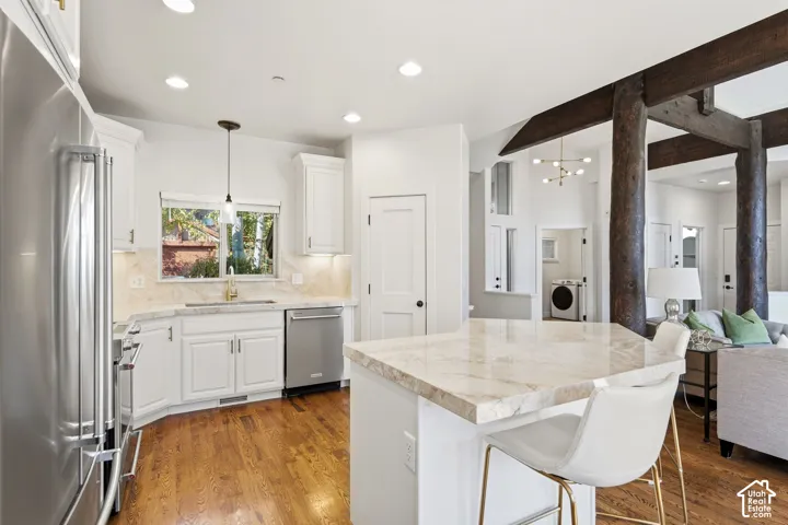 Kitchen featuring white cabinetry, stainless steel appliances, a stone countertop island, wood-finish flooring, and exposed dark wood beams