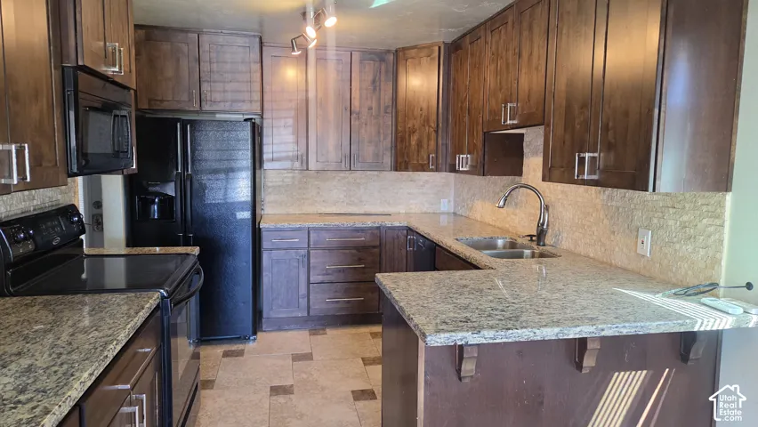 Kitchen featuring wood-finish cabinetry, granite countertops, tile backsplash, and a double basin sink with a high-arc faucet