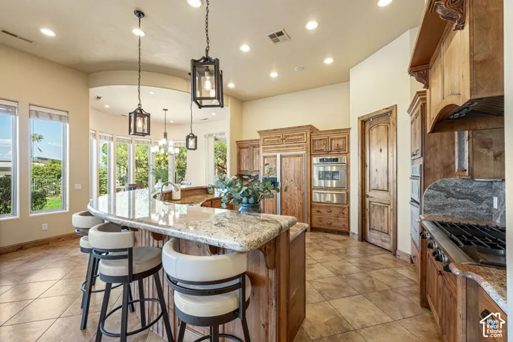 Kitchen featuring a large curved island with a stone-finish countertop, wood cabinetry, stainless steel built-in appliances, and recessed lighting