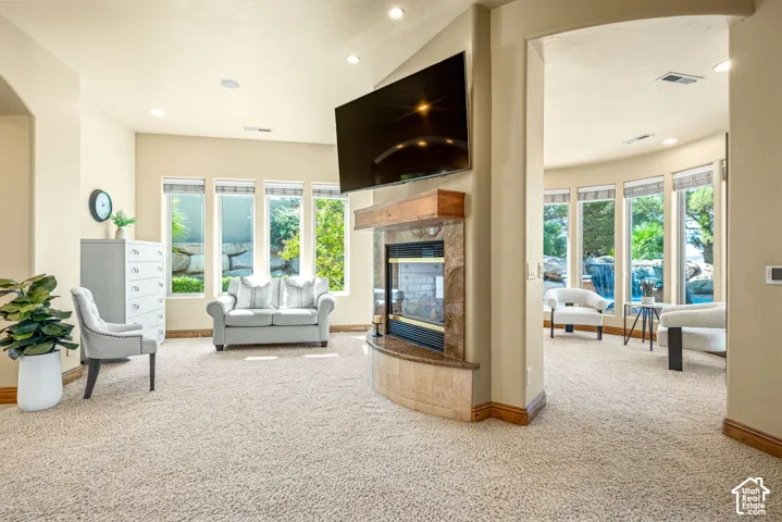 Carpeted living space featuring a built-in fireplace with a wood mantle and stone surround, recessed lighting, and multiple large windows