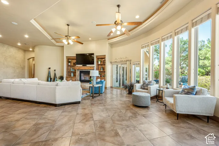 Spacious living area featuring large format tile flooring, a fireplace with built-in shelving, vaulted ceilings with recessed lighting and ceiling fans, and a wall of floor-to-ceiling windows