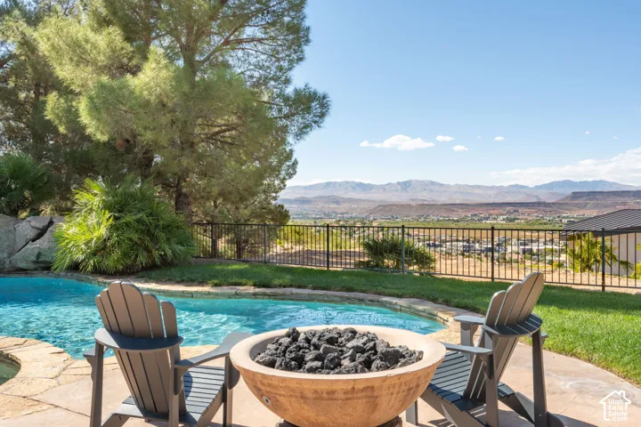 Backyard featuring a free-form pool, flagstone coping, a built-in fire pit, manicured lawn, and a black metal fence