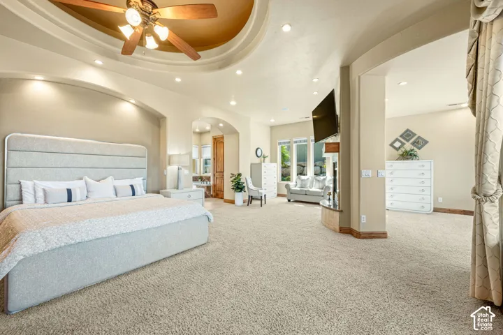Tray ceiling with recessed lighting and a ceiling fan, arched doorways, multiple large windows, and neutral carpeting