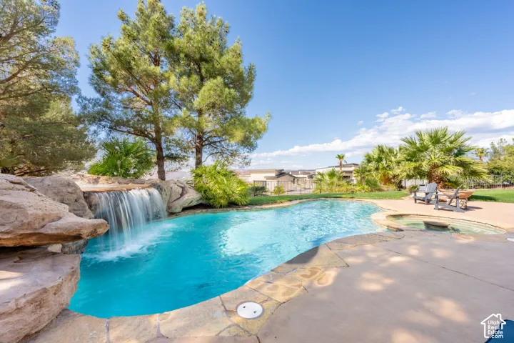 Freeform swimming pool with a rock waterfall feature, integrated spa, and expansive concrete decking