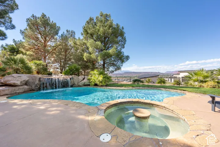 Resort-style pool with a rock waterfall feature, integrated spa, and expansive concrete decking