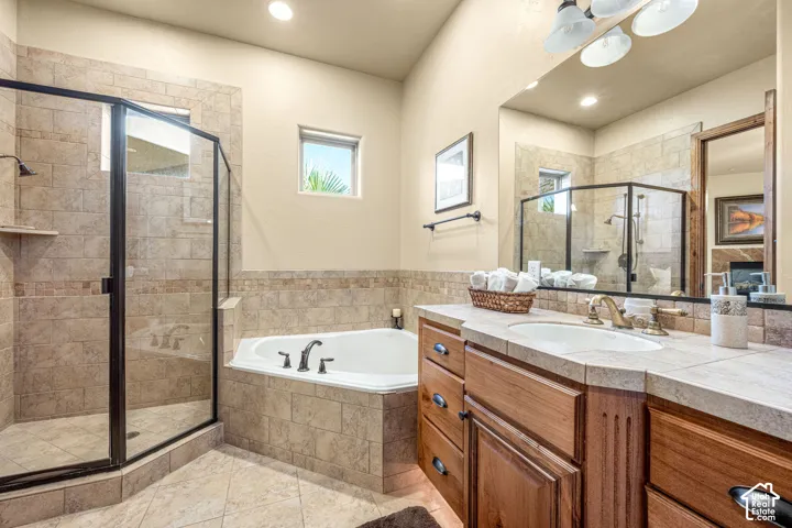 Spacious bathroom featuring a corner soaking tub, a glass-enclosed shower, a wood-finish vanity with an integrated sink, and tiled flooring