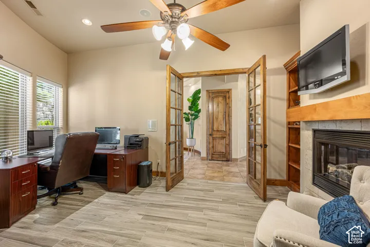 Wood-finish tile flooring throughout, wood-framed French doors, ceiling fan with integrated lighting, recessed lighting, and a built-in fireplace with a wood mantel
