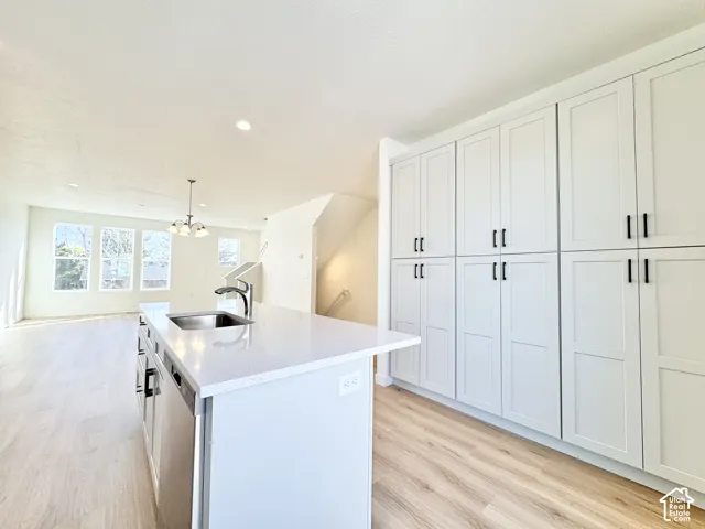 Spacious kitchen island with an undermount sink, ample white cabinetry, wood-finish flooring, and recessed lighting