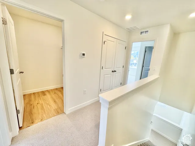 Carpeted hallway featuring a built-in storage closet with wood-finish flooring, recessed lighting, and a thermostat