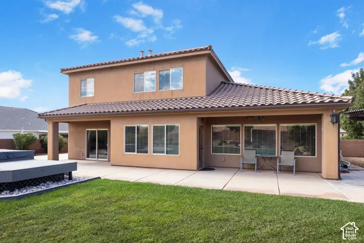 Two-story stucco exterior with a tile roof, covered patio, multiple windows, and a raised composite deck