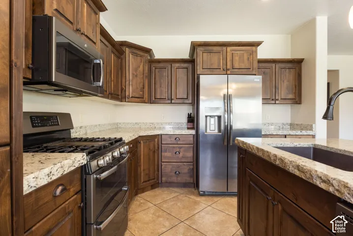 Kitchen featuring wood cabinetry, light-colored countertops, stainless steel appliances, and tile flooring