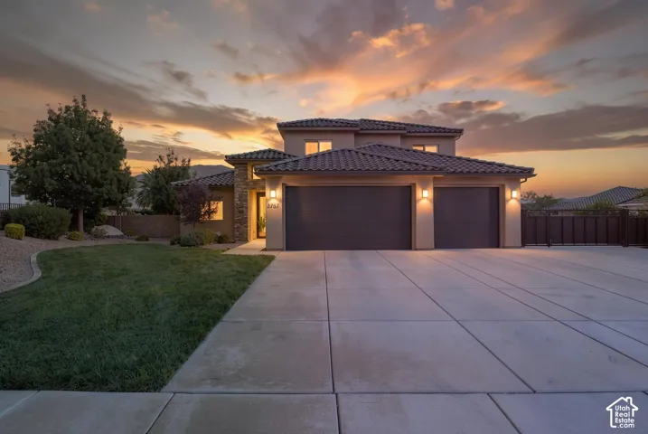 Stucco exterior with stone accents, tile roof, two-car garage, large concrete driveway, and manicured landscaping