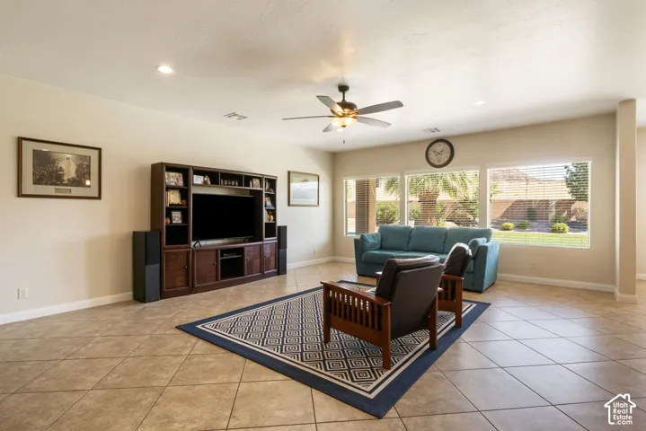 Spacious living area showcasing tile flooring, a ceiling fan with integrated lighting, built-in entertainment cabinetry with display shelving, and expansive windows framing natural light and outdoor scenery
