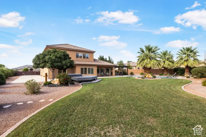 Expansive backyard featuring a manicured lawn, paved patio, swimming pool, and mature palm trees