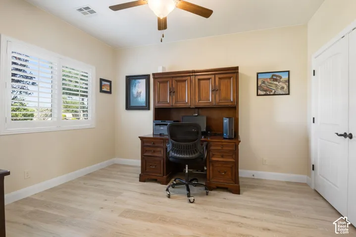 Light-toned wood-finish flooring, white plantation shutters, and a ceiling fan with integrated lighting